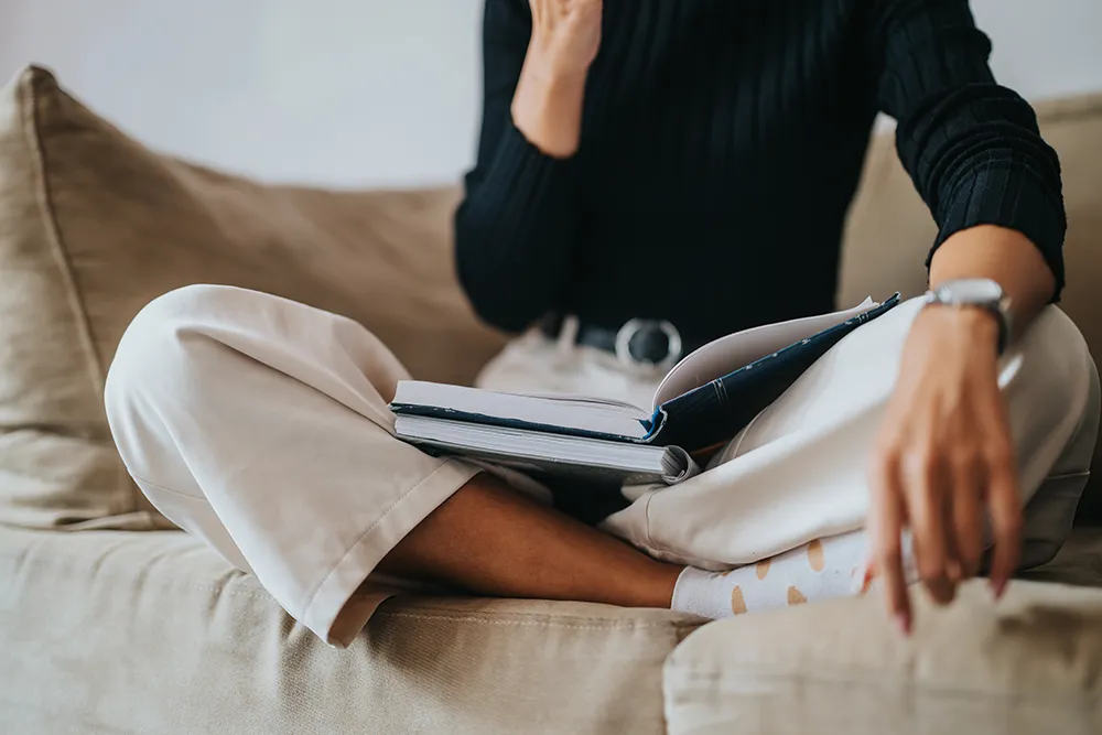 Person sitzend auf Sofa mit Büchern (Symbolbild)